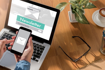 Person hält Smartphone mit E-Mail-Symbol vor Laptop mit „Newsletter YOUR E-MAIL“ auf dem Bildschirm.